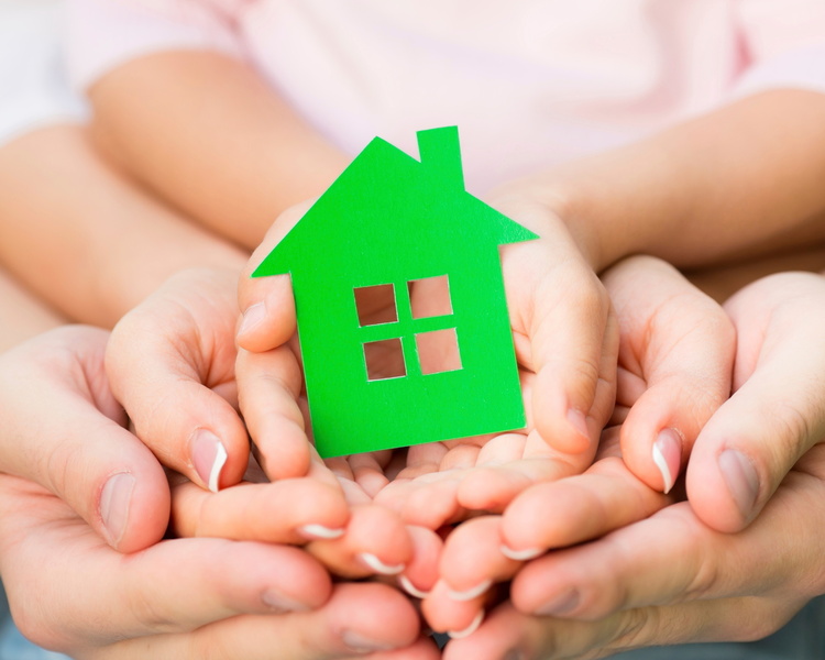 Family holding green paper house in hands. Real estate concept
