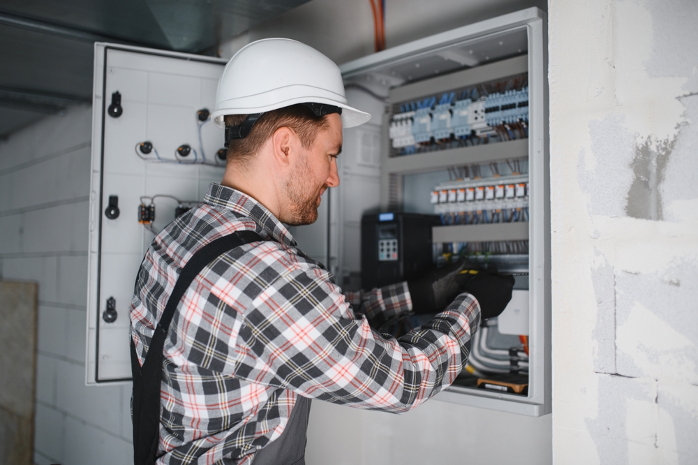 Electrician wearing safety helmet replacing electric control panel.